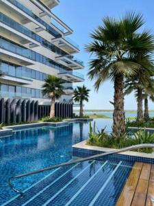 une piscine avec des palmiers devant un immeuble dans l'établissement Yas Island Resort Beach Access Luxury in Mayan 1 BEDROOM, à Yas Island