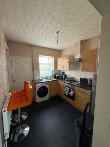 a small kitchen with an orange chair and a stove at Cosy Room Near Train & Hospital 
