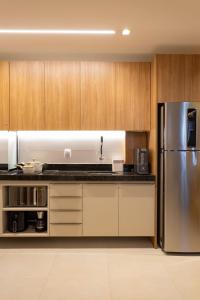 a kitchen with wooden cabinets and a stainless steel refrigerator at Studio Moderno e Aconchegante | Pajuçara - Maceió in Maceió
