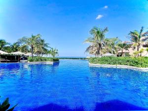 a large swimming pool with palm trees and the ocean at Villa Private Pool in Cam Lâm