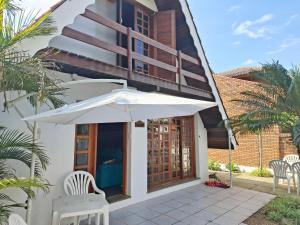 a white umbrella and chairs in front of a building at Linda Cabana 3 Quartos a 50m da Praia in São Lourenço do Sul