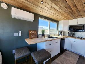 a kitchen with white cabinets and a counter with two stools at Stunning Tiny House with Picnic Space, Barbecue and Fire Pit in Meadview, Arizona in Ray Place