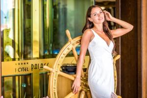 een vrouw in een witte jurk die naast een houten wiel staat bij Hotel Palace Marina Dinevi in Sveti Vlas