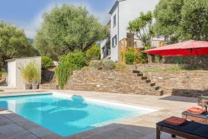 una piscina con un ombrellone rosso accanto a un edificio di Villa Le Corps de Garde a Furiani