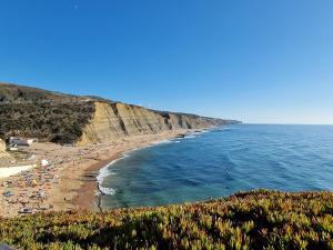 una playa con un montón de gente y el océano en Magoito Beach-Beautiful Walkways and Fossil Cliffs, en São João das Lampas