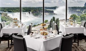 a restaurant with white tables and chairs and a view of niagara falls at The Brock Niagara Falls Fallsview, Tapestry by Hilton in Niagara Falls