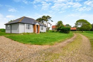 a small white house on a grassy field with a dirt road at Lodge Farm Cottage in Sudbourne