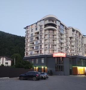 a large apartment building with two cars parked in a parking lot at Апартаменти ЖК Скеля in Yaremche +2 photos