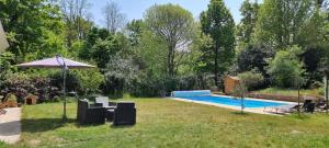 a backyard with a swimming pool and an umbrella at Campagne et bien être - Collection Idylliq in Villiers-sous-Grez