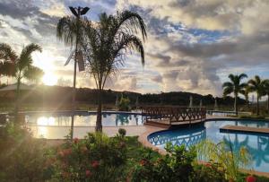 a resort swimming pool with a palm tree and the sunset at Village em Barra do Jacuípe in Camaçari