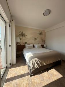 a bedroom with a large bed with palm trees on the wall at Charm-In Apartments in Vila Nova de Milfontes