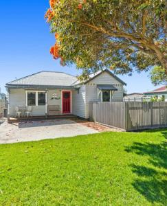a house with a red door and a fence at Mini Beach Cottage - Seaspray Escape in Seaspray