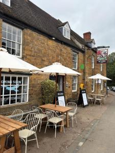 mesas e cadeiras com guarda-sóis em frente a um edifício em The George Inn em Lower Brailes
