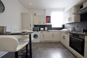 cocina con armarios blancos, mesa y lavavajillas en NEST SUITE Studio Flat in North London, en Londres