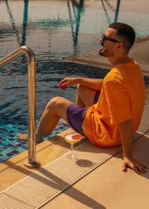 a man sitting on the edge of a swimming pool at Mövenpick Hotel & Apartments Ghala Muscat in Muscat