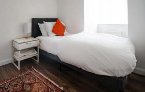 a bed with white sheets and an orange pillow on it at Relaxing 5BDR Retreat Hot Tub in Allesley