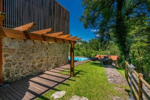 a wooden pergola next to a wall with a swimming pool at Moinhos do Coto in Vila Verde