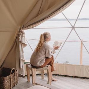 a woman sitting on a stool reading a book in a tent at Rum Monet in Disah