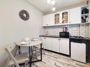 une cuisine avec des placards blancs et une petite table et une chaise blanches dans l'établissement Арбат в Золотом квадрате двухкомнатная стильная в центре 25, à Almaty