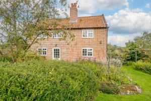 ein altes rotes Backsteinhaus auf einem grünen Feld in der Unterkunft Riverside Cottage in Snape