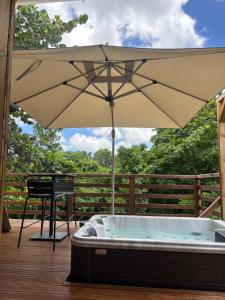 a hot tub with an umbrella on a deck at La pause verte bungalow in Sainte-Anne