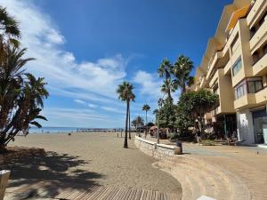 a sandy beach with palm trees and a building at Sea View Penthouse Apartment with Hot Tub - Casa Bella Vista, Buenas Noches , Estepona in Estepona