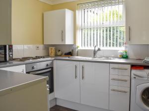 eine Küche mit weißen Schränken und einer Spüle und einem Fenster in der Unterkunft Bramley Lodge Annex in Clenchwarton