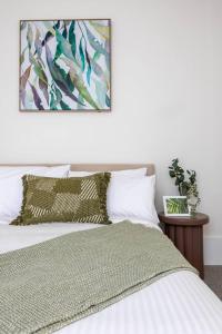 a bedroom with a bed with white sheets and a painting at The Lightwell - Sunlit Beachside Escape with Rooftop in Melbourne