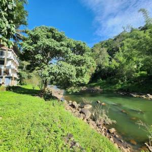Un río al lado de una colina con árboles y un edificio. en John's Heaven Valley, en Idukki