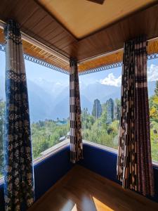 a room with a large window with mountains in the background at The District Green in Kalpa