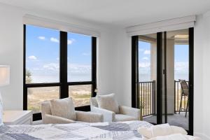 a bedroom with a bed and two chairs and windows at Summer House 202 - 3BR Oceanfront Condo! View! in Isle of Palms