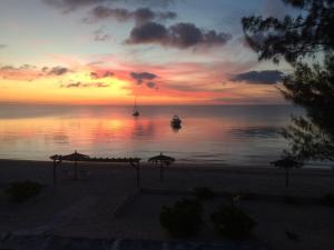a sunset on the beach with a boat in the water at Cocodimama small - Boutique Resort on Spectacular Beach Hotel Room in Governors Harbour