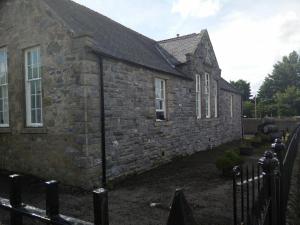 een oud stenen huis met een hek ervoor bij The Smugglers Hostel in Tomintoul