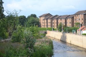 a river in front of a brick building with a bridge at Boat Green Apartment in Edinburgh