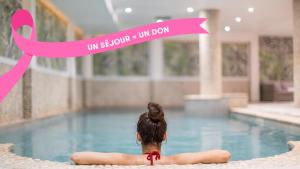 Una mujer sentada en una piscina con un lazo rosa. en Urban Hotel & Spa Aix-les-Bains - BW Signature Collection, en Aix-les-Bains