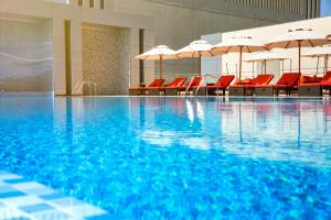 a swimming pool with red chairs and umbrellas at Downtown Rotana in Manama