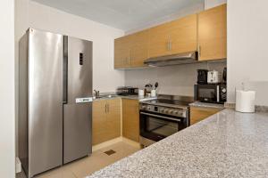 a kitchen with a stainless steel refrigerator and wooden cabinets at Silkhaus Premier 2BR Apartment in Marina Bay in Mushayrib