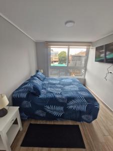 Un dormitorio con una cama con edredón azul y una ventana. en Movistar Arena - Ohiggins Park - Parking, en Santiago