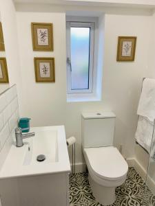 a white bathroom with a toilet and a window at 2 bedroom cottage in Bromley suitable for 4 people in Bickley