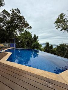 a blue swimming pool with a wooden deck and trees at Toninhas Beach - Gated Community - Ubatuba-SP in Ubatuba