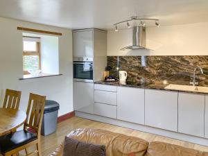 a kitchen with white cabinets and a table and a couch at The Milking Parlour in Alston