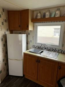 a kitchen with a white refrigerator and a window at Coastfield Holiday Village - Holiday Accommodation 17403 in Ingoldmells +4 photos