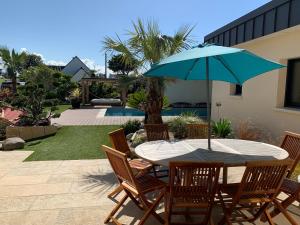 une table et des chaises avec un parapluie bleu dans l'établissement VILLA de Standing, 10 personnes, Piscine, Spa à 200m des plages, à Brignogan-Plage