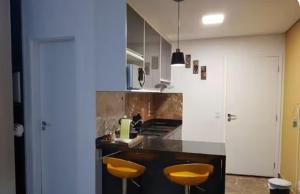 a kitchen with two yellow stools and a counter at Flat Novo1 - Café, Cama Queen, Ar, Estac e Internet in Barueri