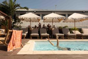 a person swimming in a pool with chairs and umbrellas at Drifter Byron Bay in Byron Bay