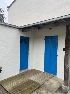 Un edificio blanco con puertas azules y un porche de madera. en Chez Jean-Jean, en Chantonnay