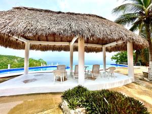 a pavilion with chairs and a table and a straw umbrella at Bungalow frente a la playa estrene alberca nueva con increíble vista infinita al mar, 8 hermosas playas cercanas, terraza con cama de playa, espectacular vista al inmenso océano pacífico, 2 kayack disponibles, nómadas digitales Starlink WiFi 224 mbps in Puerto Ángel