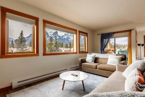 a living room with a couch and a table and windows at Bluebird - Spacious Luxury Shared Rooftop Hot Tub in Canmore