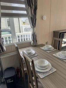 a dining room table with plates and chairs and a window at Spacious Modern Seaside Caravan in Lossiemouth +10 photos