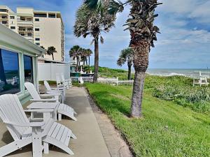 a patio with white chairs and palm trees and the ocean at Sunrise Cottage by the Sea in Ormond-by-the-Sea +31 photos